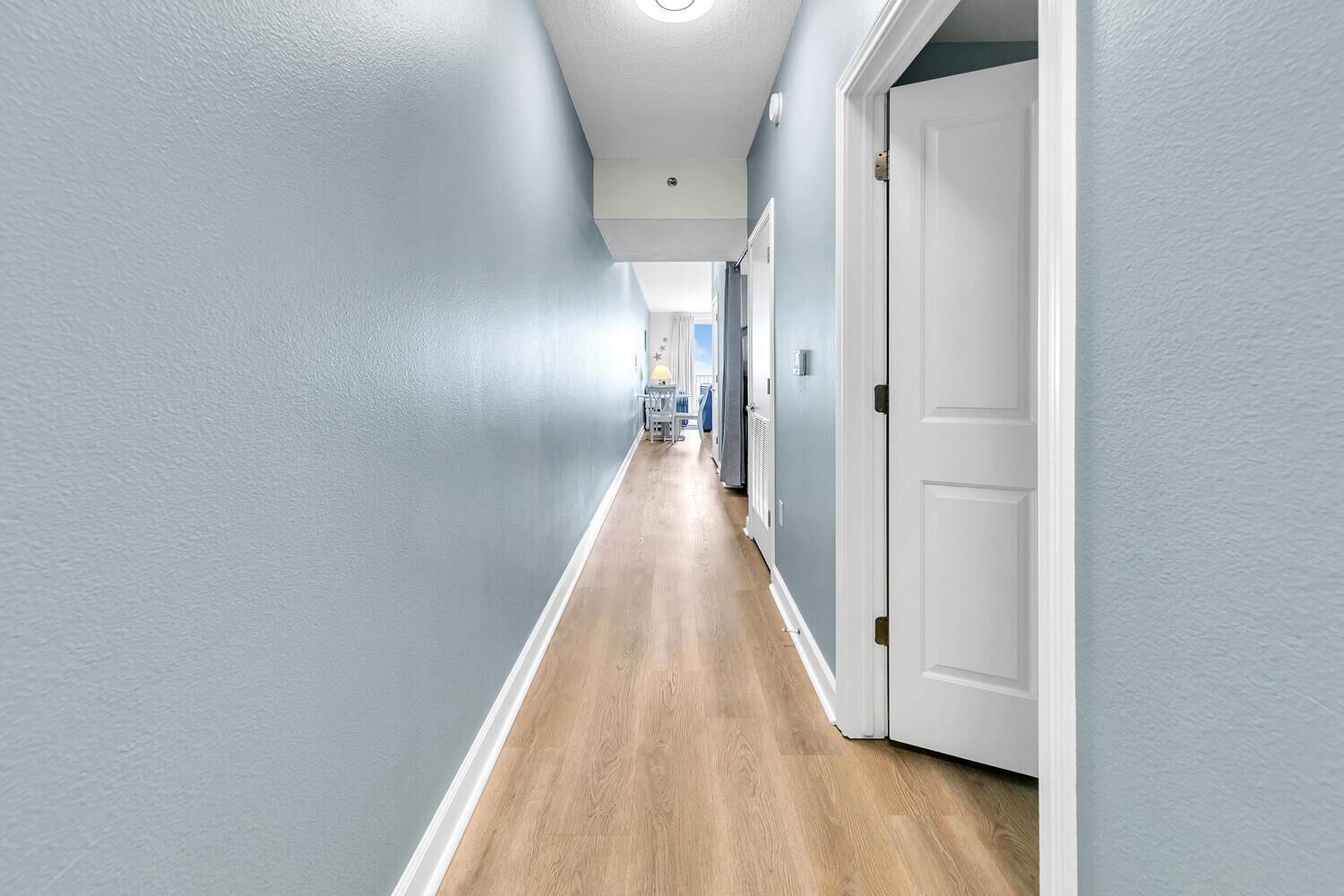 Un pasillo con paredes azul claro, suelo de madera y puertas blancas.
