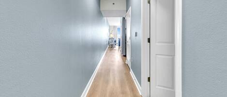 Un pasillo con paredes azul claro, suelo de madera y puertas blancas.