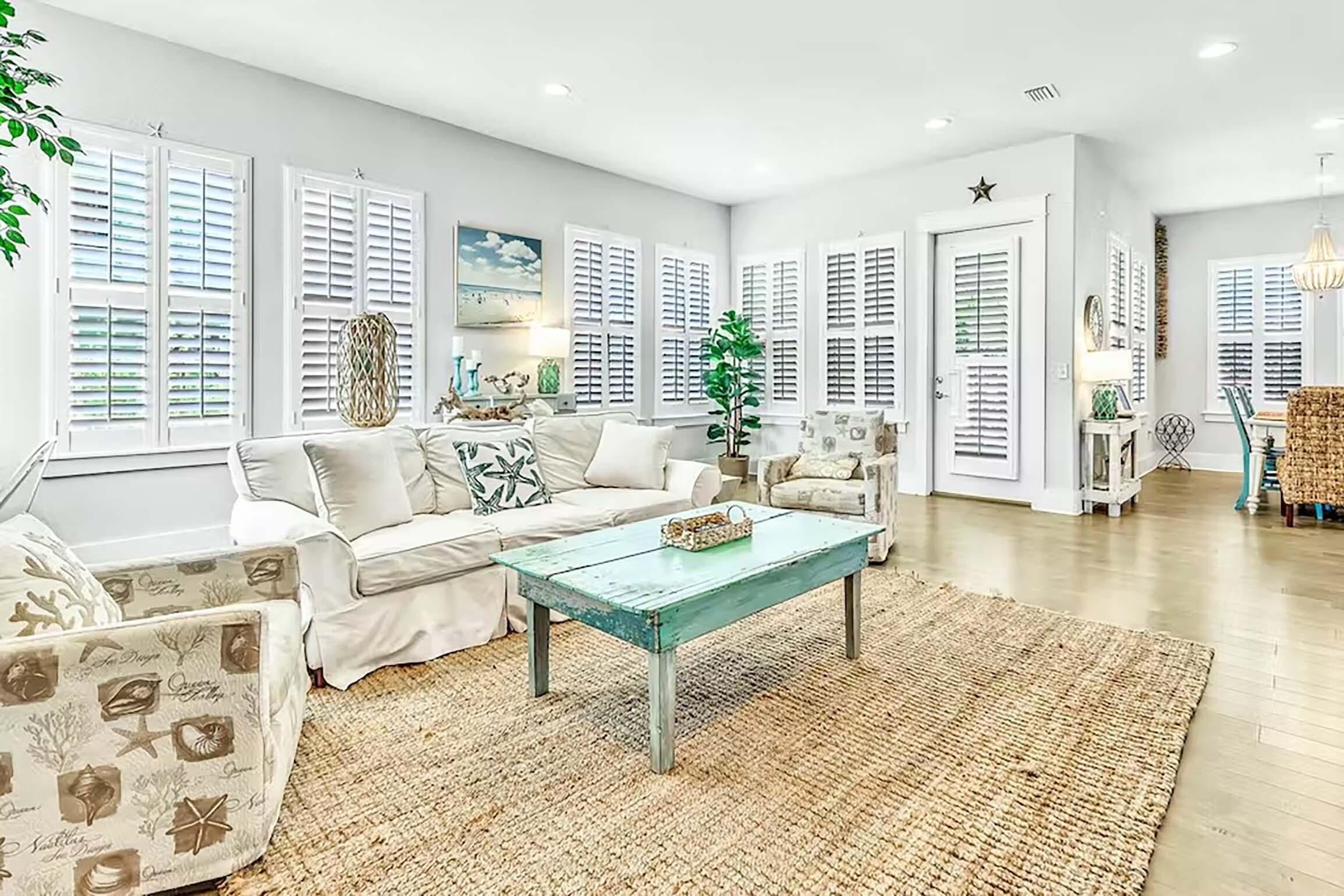 A spacious living room with a light-colored sofa, a coffee table, and a large window with shutters.