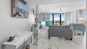 Ein modernes Wohnzimmer mit grauem Sofa, einem weißen Konsolentisch, einem großen Spiegel und Meerblick durch große Fenster.