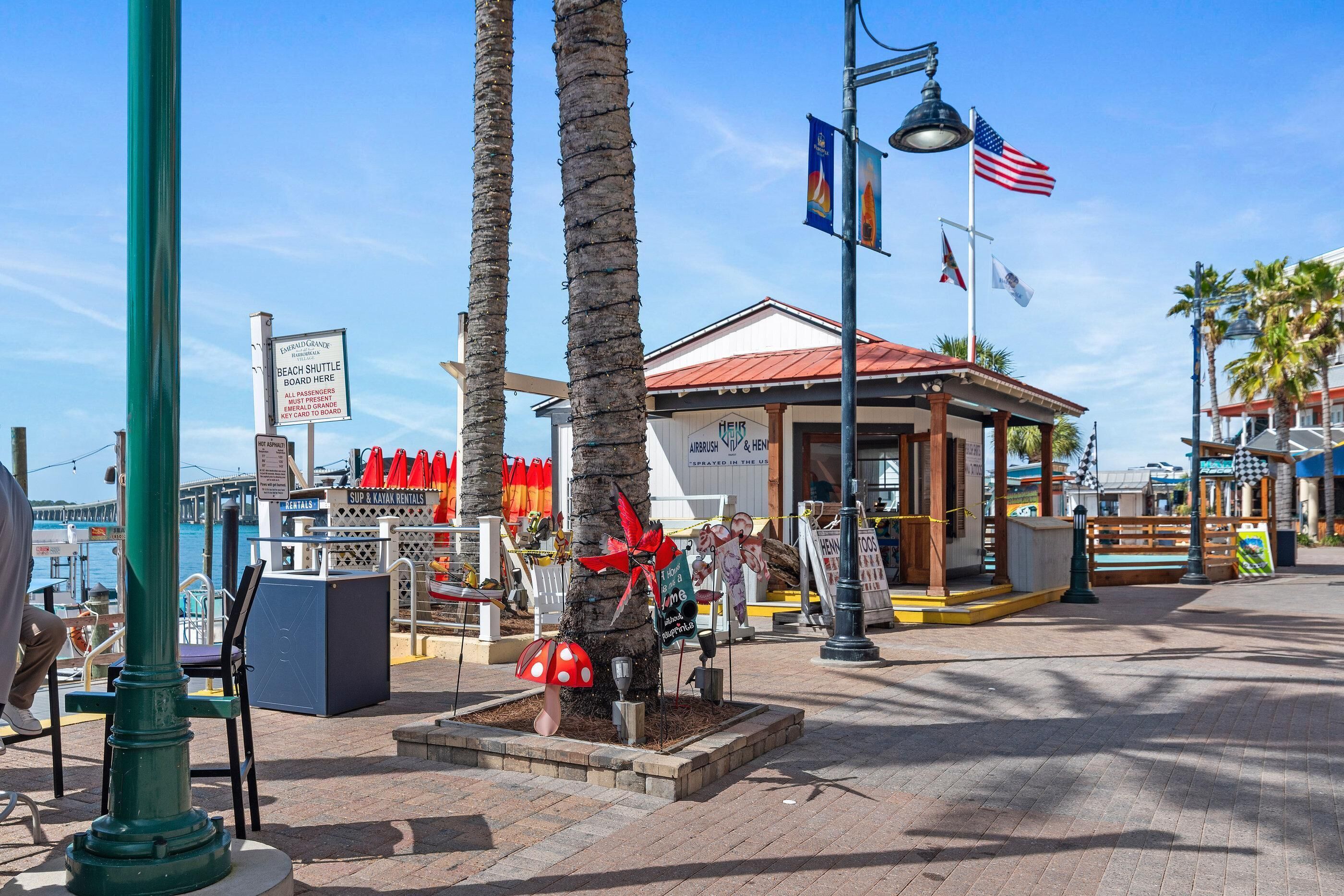 A beachside area with a boardwalk, palm trees, and a small pavilion with flags.