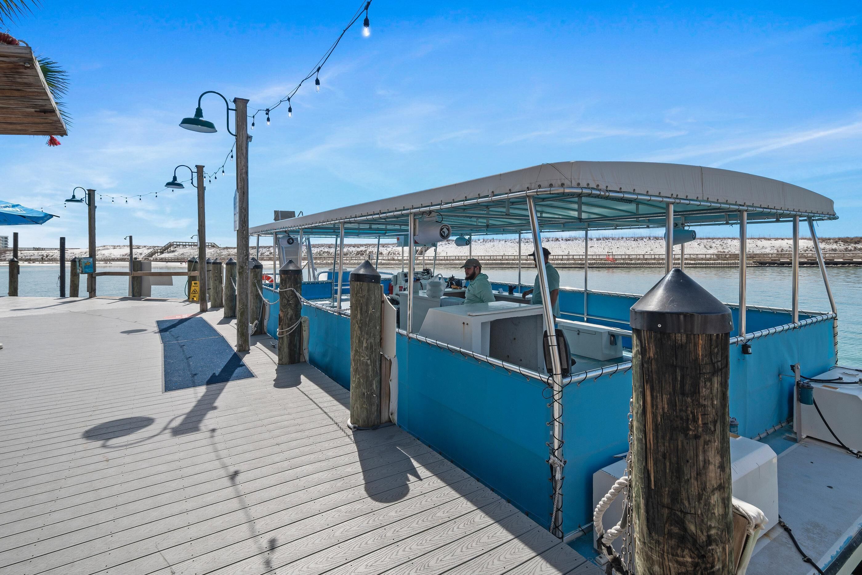 A boat docked at a pier with a covered seating area, a wooden deck, and a clear view of the water.