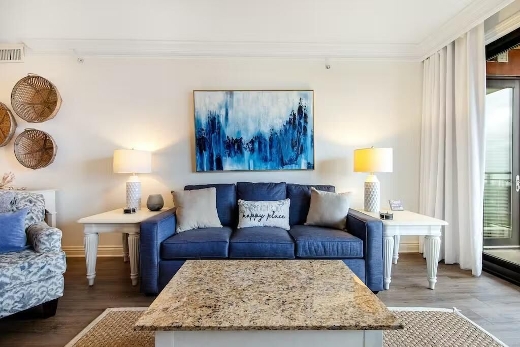 A modern living room with a blue sofa, two side tables with lamps, a coffee table, and a large abstract painting on the wall.