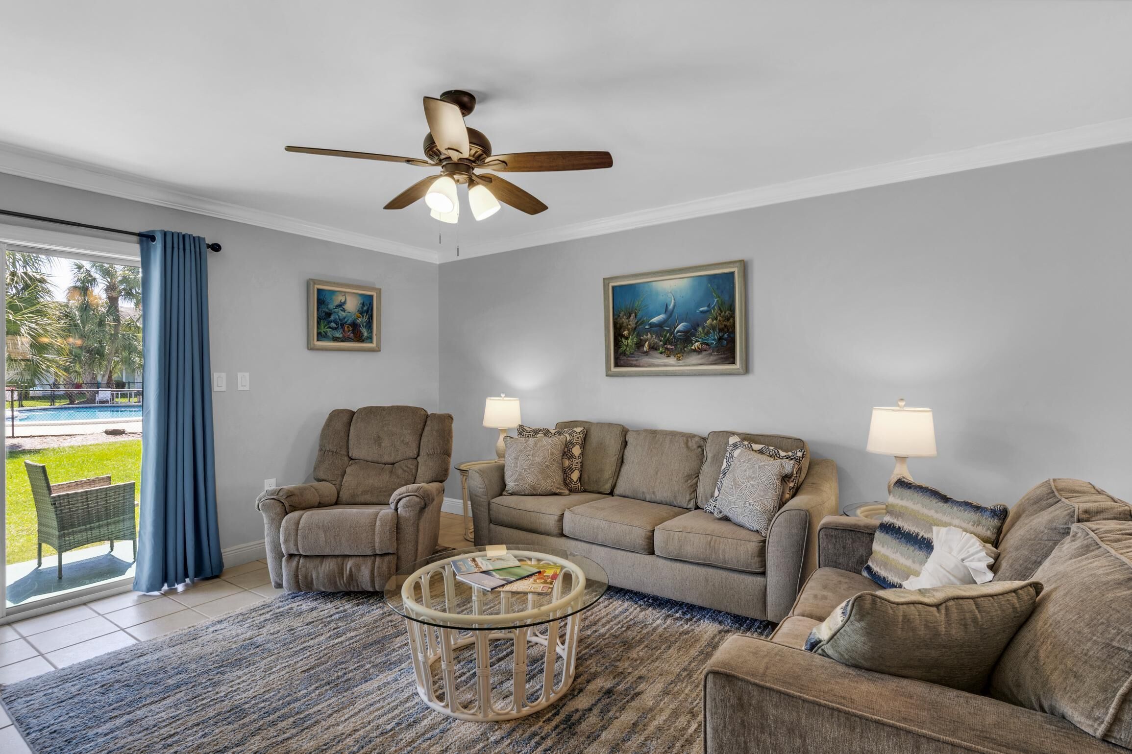 A living room with a ceiling fan, two couches, a coffee table, and a view of a pool outside.