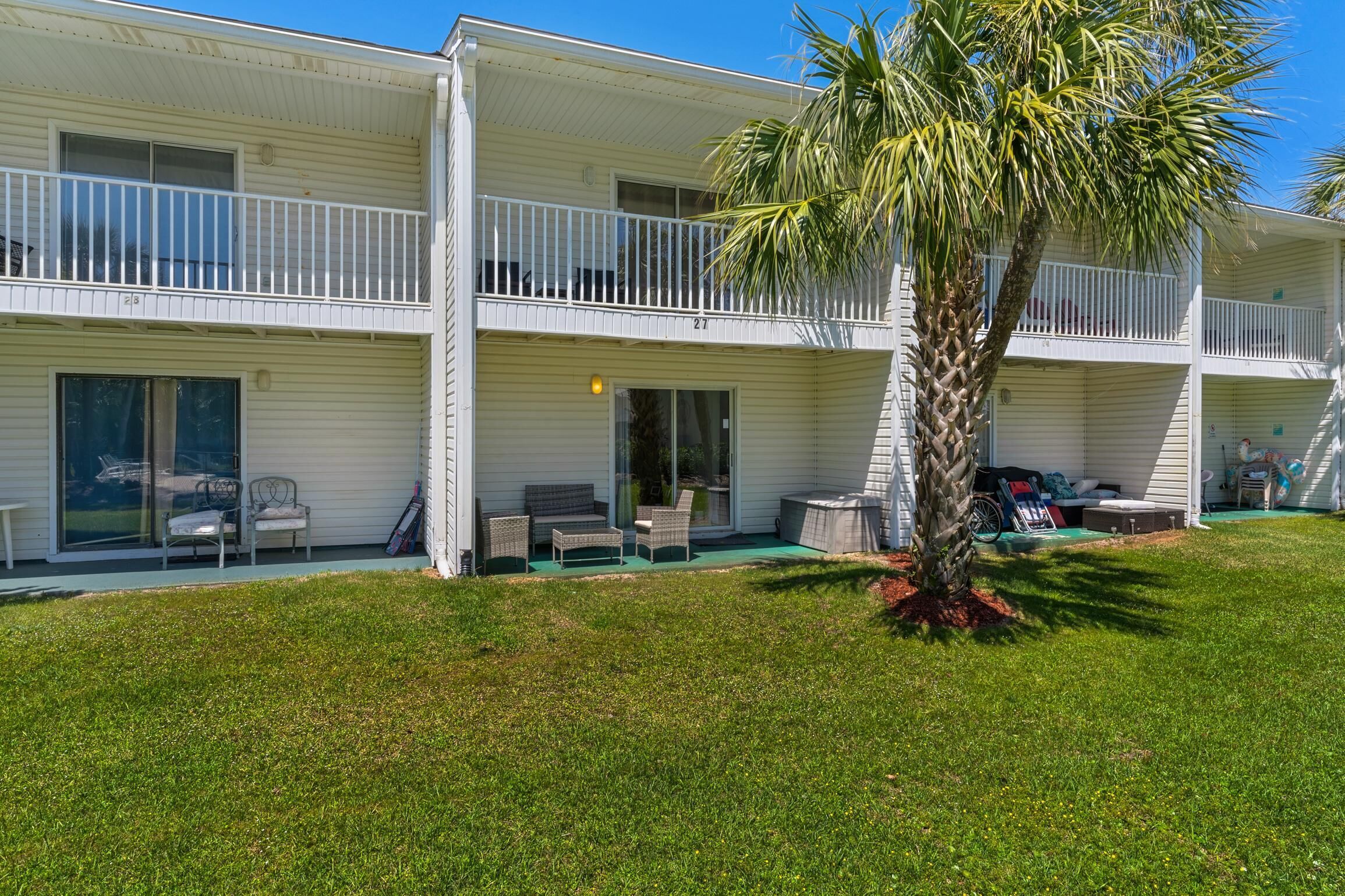 A two-story motel with a balcony, outdoor seating, and a palm tree.