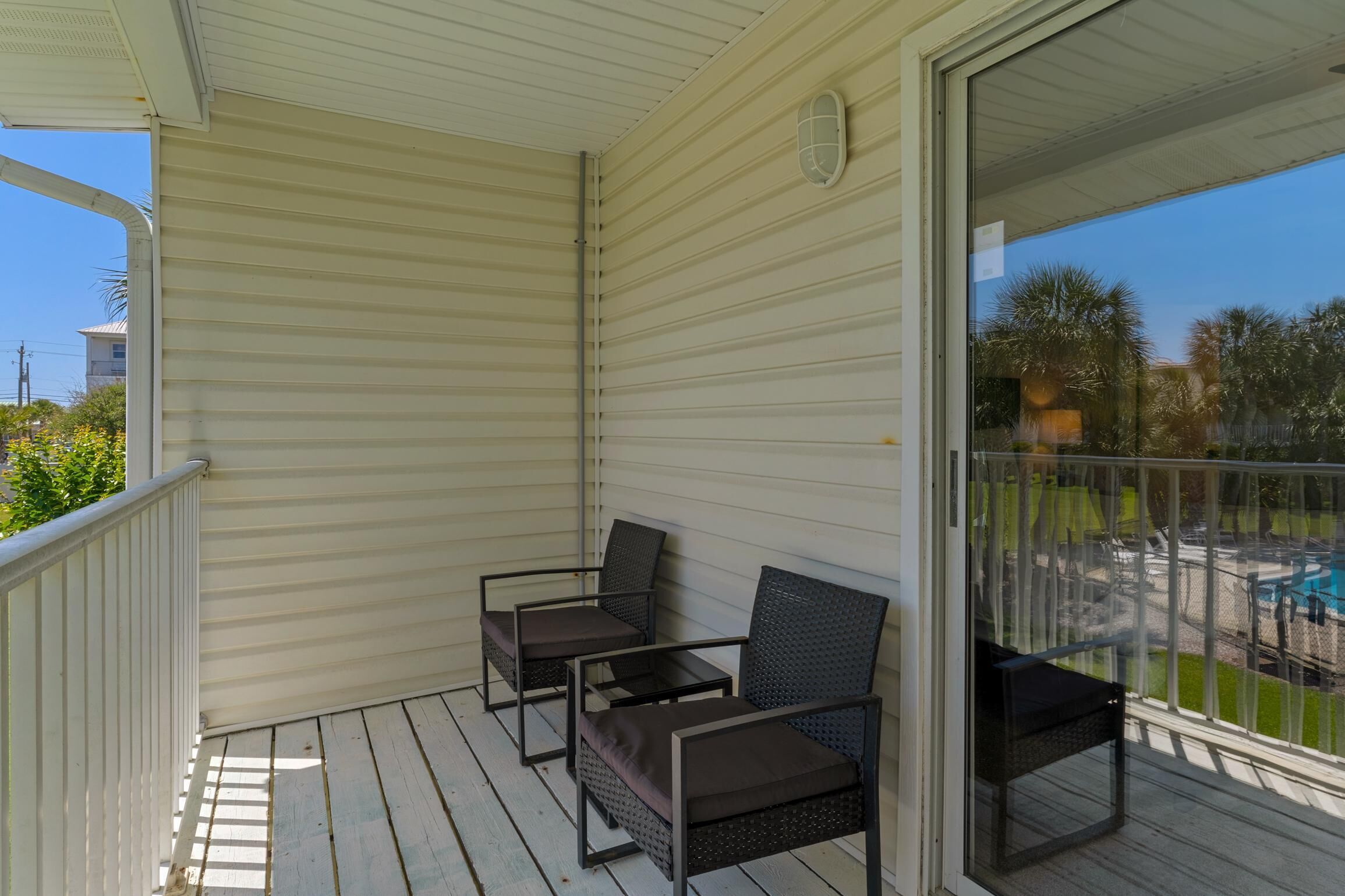 A covered balcony with two chairs and a table, overlooking a swimming pool and greenery.