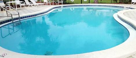 A swimming pool with a tiled edge, surrounded by lounge chairs and a stone-tiled deck.