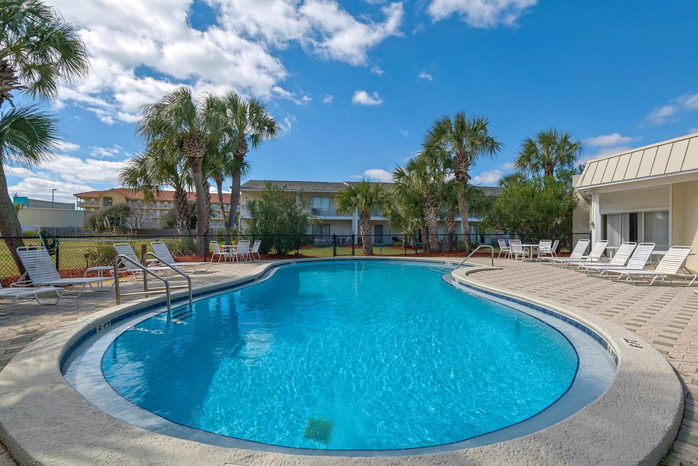 A swimming pool with lounge chairs, palm trees, and a building in the background.