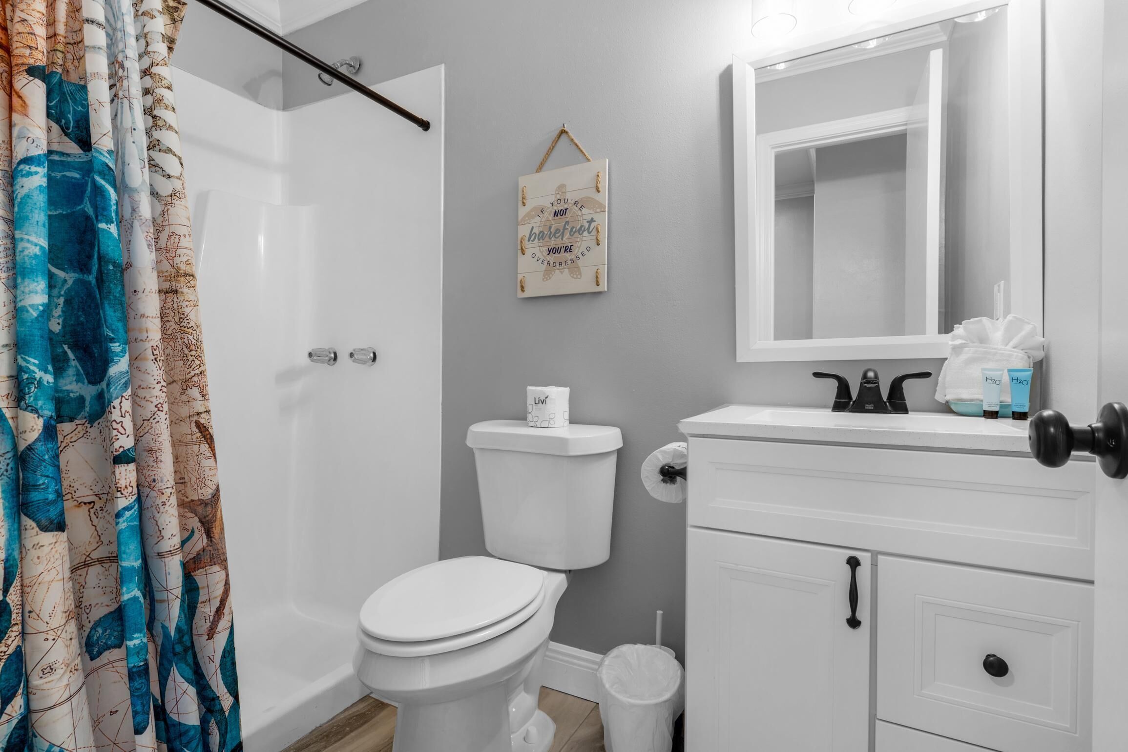 Une salle de bain équipée de toilettes, d’un rideau de douche, d’une enseigne suspendue, d’un miroir et d’un lavabo avec des articles de toilette.