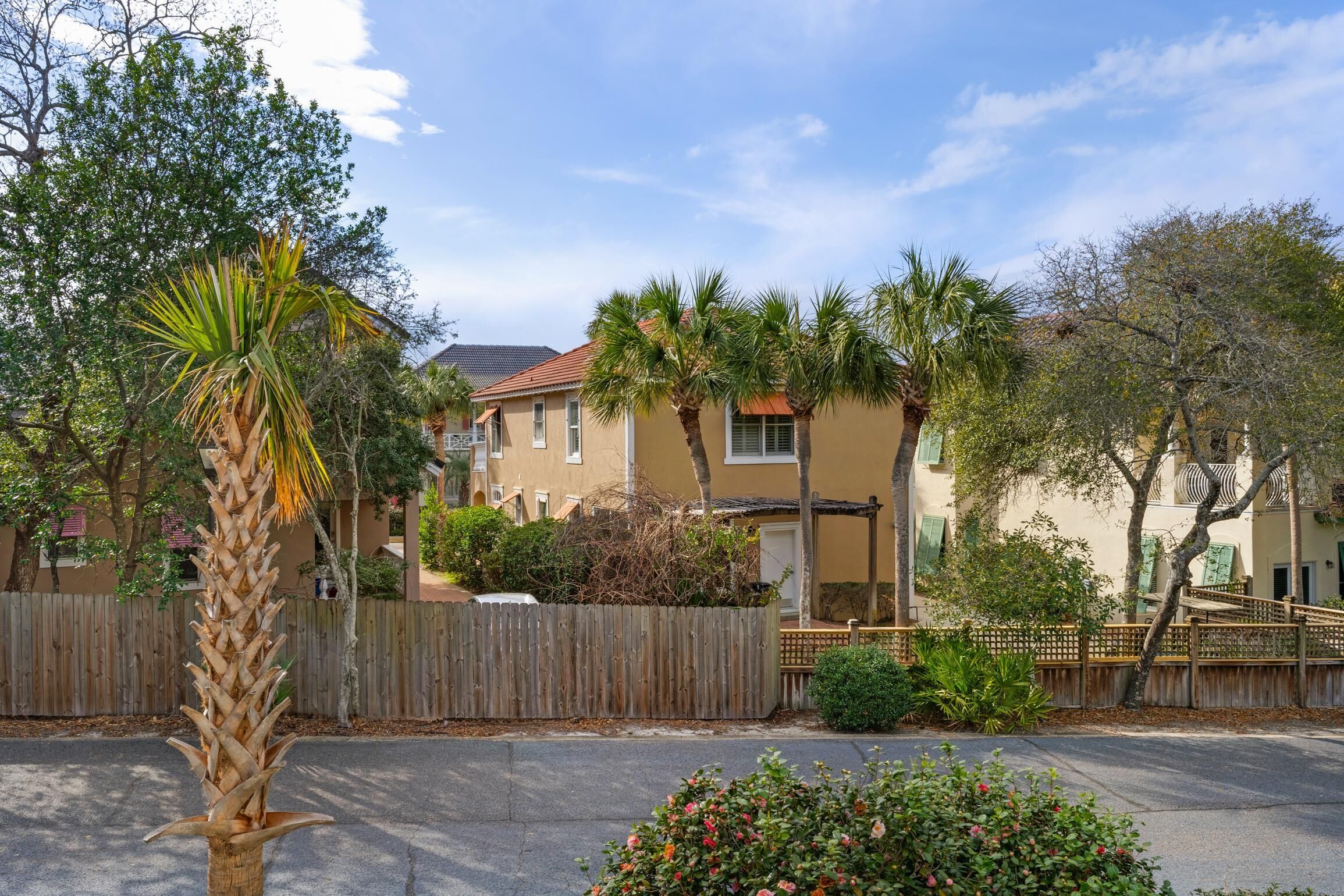 A residential area with a beige house, palm trees, and a wooden fence.