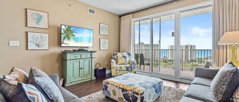 A spacious living room with a large window, a ceiling fan, and a flat-screen TV.