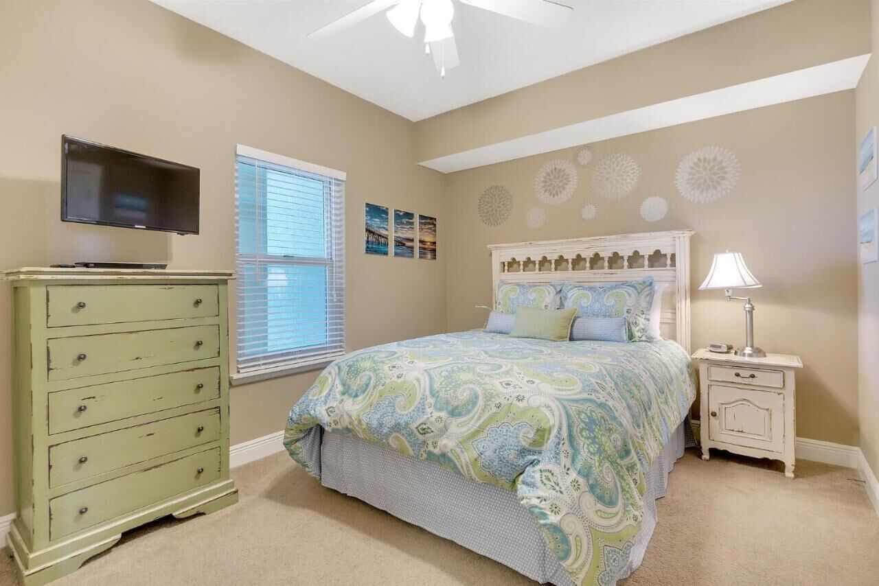 A bedroom with a bed, dresser, TV, window, and decorative wall art.