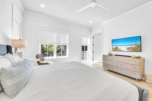 Une chambre spacieuse avec un grand lit, une commode, un téléviseur et une vue sur l’extérieur par les fenêtres.