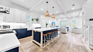 Uma cozinha moderna com armários brancos, uma ilha central com banquetas e iluminação pendente.