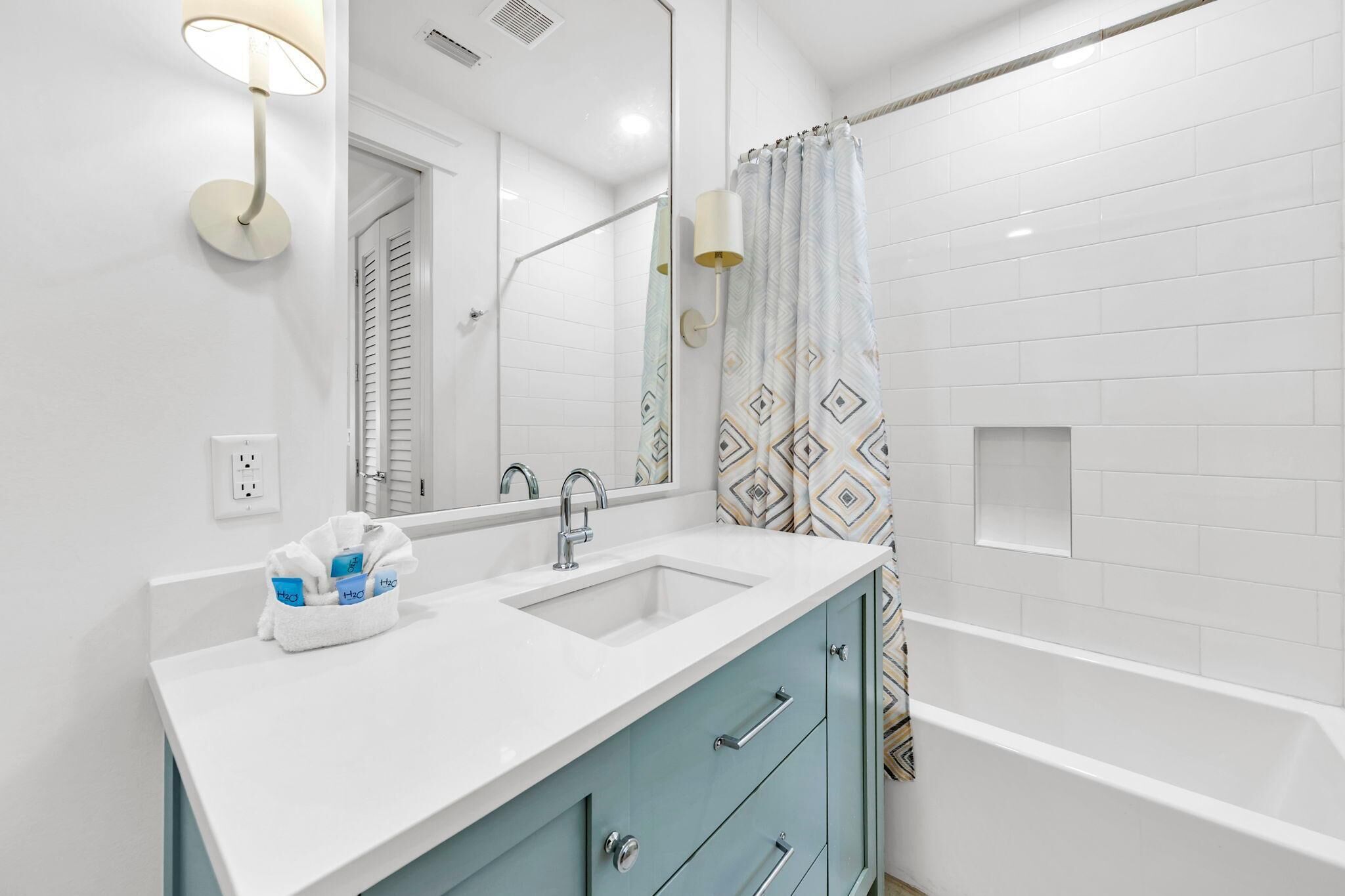 A modern bathroom with a white sink, two mirrors, a blue cabinet, and a shower curtain with a geometric pattern.