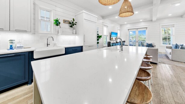 Cozinha moderna com uma ilha grande, armários brancos e vista para a sala de estar.