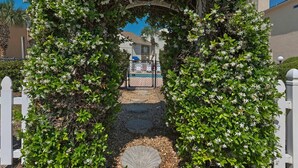 An archway covered in flowering plants leading to a gated area.