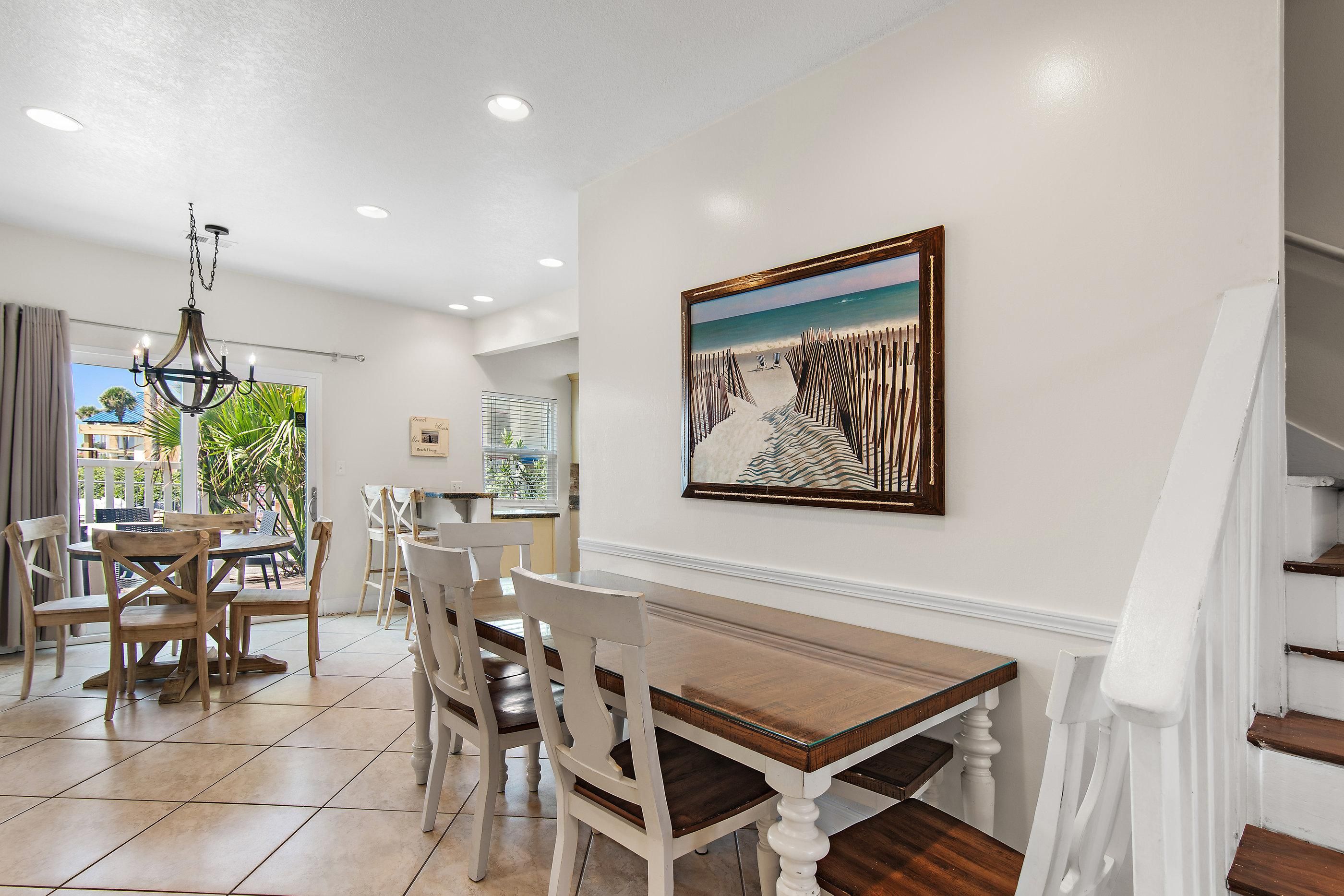 A dining area with a wooden table and chairs, a chandelier, and a painting of a beach scene on the wall.