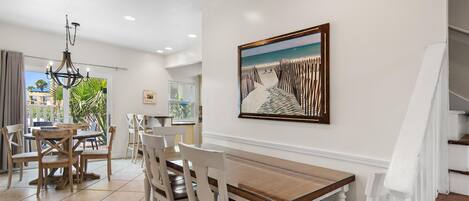 A dining area with a wooden table and chairs, a chandelier, and a painting of a beach scene on the wall.