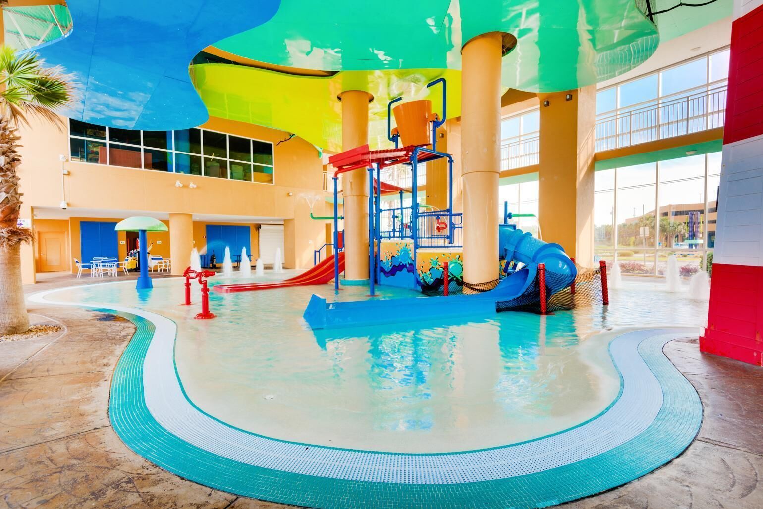 Ein Wasserpark im Innenbereich mit Rutschen, einem Schwimmbecken und einem überdachten Bereich mit Sitzgelegenheiten.