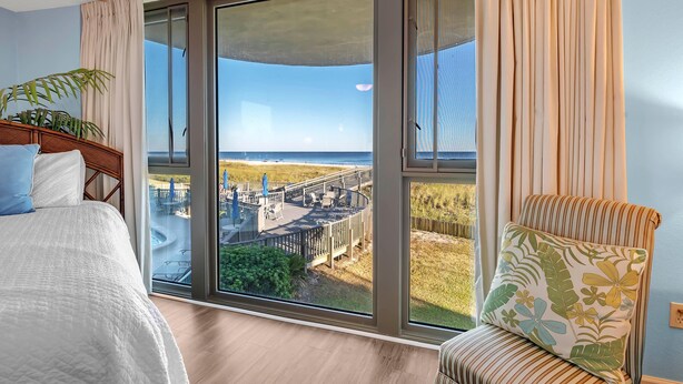 Une chambre d’hôtel dotée d’une grande porte-fenêtre coulissante donnant sur un balcon avec vue sur une plage et une promenade en bord de mer.