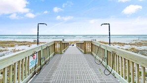 Une promenade en bois mène à une plage, et un panneau indique que l’eau se trouve à environ 30 mètres.