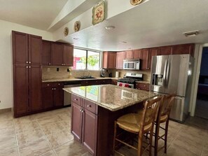 A kitchen with dark wooden cabinets, a granite countertop, stainless steel appliances, and a large island with two chairs. - 12 guests. W/ Ping pong, Air hockey, Volleyball! (Las Vegas)