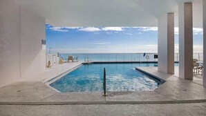An indoor swimming pool with a view of the ocean, surrounded by white pillars and a clear sky. - Windemere 1204 (Pensacola)
