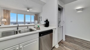 A modern kitchen with a dishwasher, double sink, and a view of the ocean. - Windemere 1204 (Pensacola)