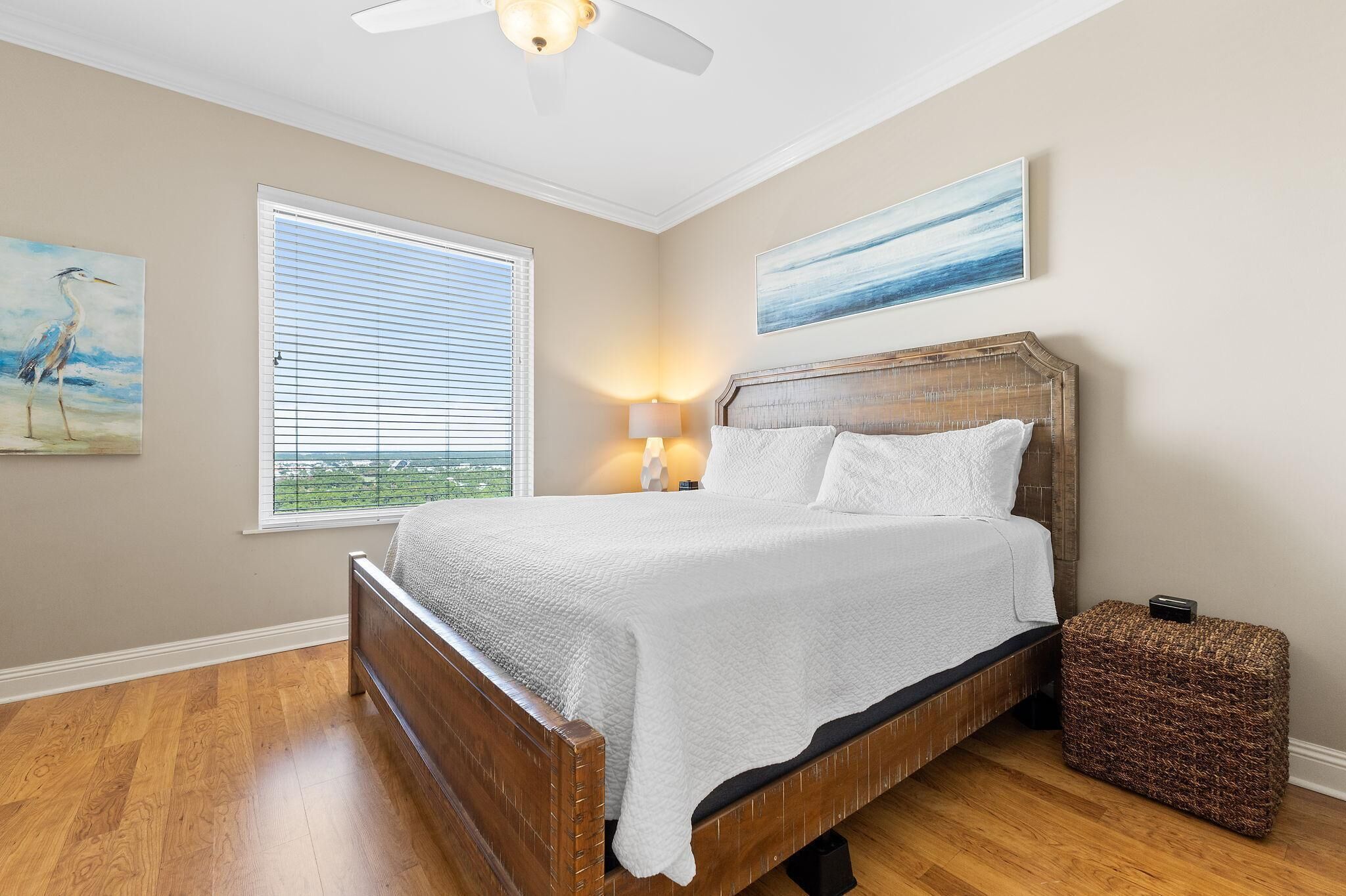 A bedroom with a wooden bed, a window with blinds, a ceiling fan, and a nightstand with a lamp.