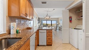 A modern kitchen with granite countertops, wooden cabinets, and a built-in dishwasher. - Shipwatch B101 (Pensacola)