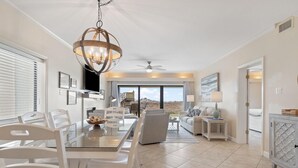 A spacious living room with a dining area, a chandelier, and a view of the outdoors. - Shipwatch B101 (Pensacola)