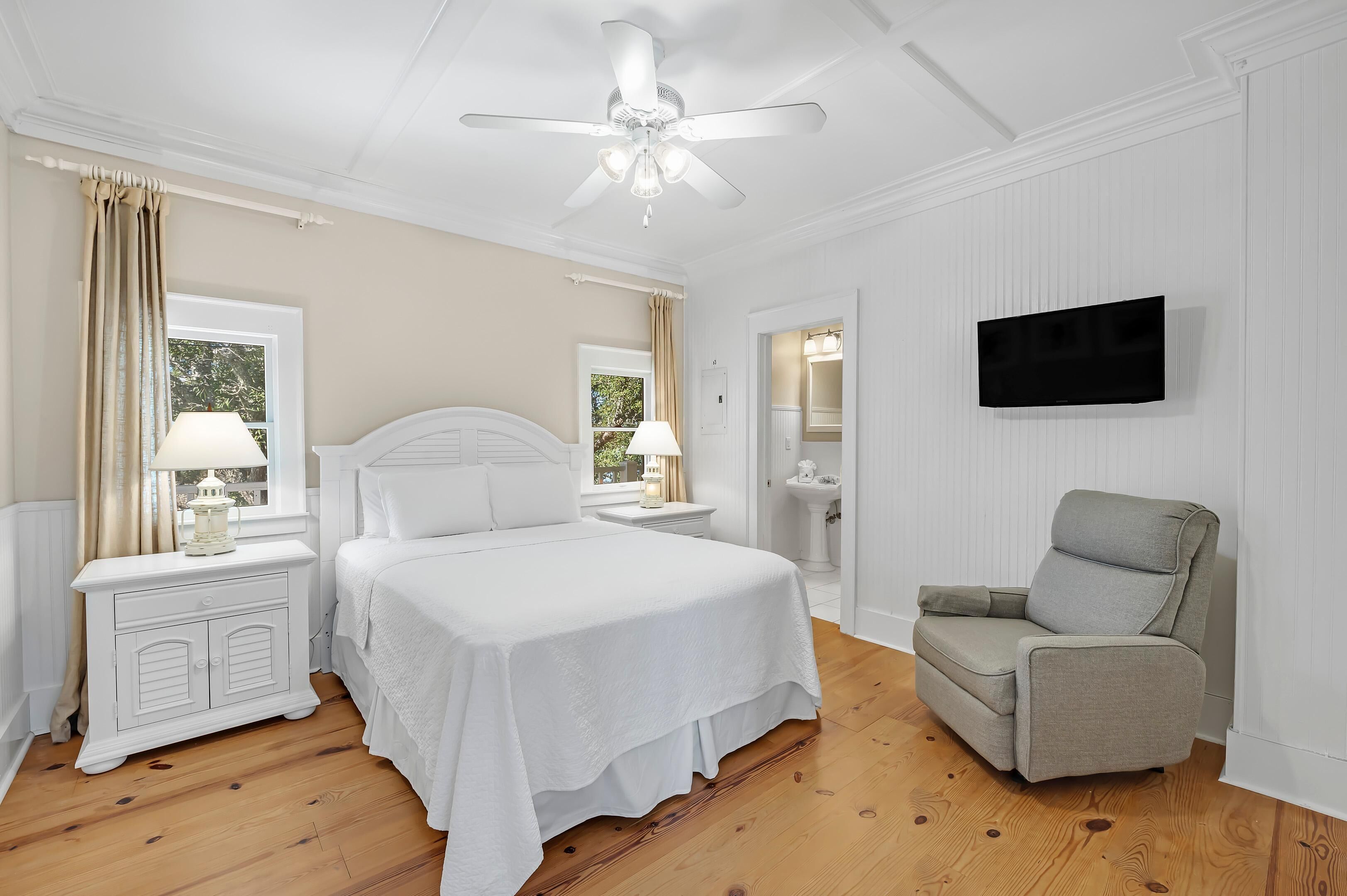A bedroom with a bed, nightstands, a chair, a ceiling fan, and a TV.