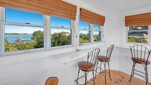 A room with three large windows, a white interior, and a view of a body of water and buildings. - Ole River Cottage (Pensacola)