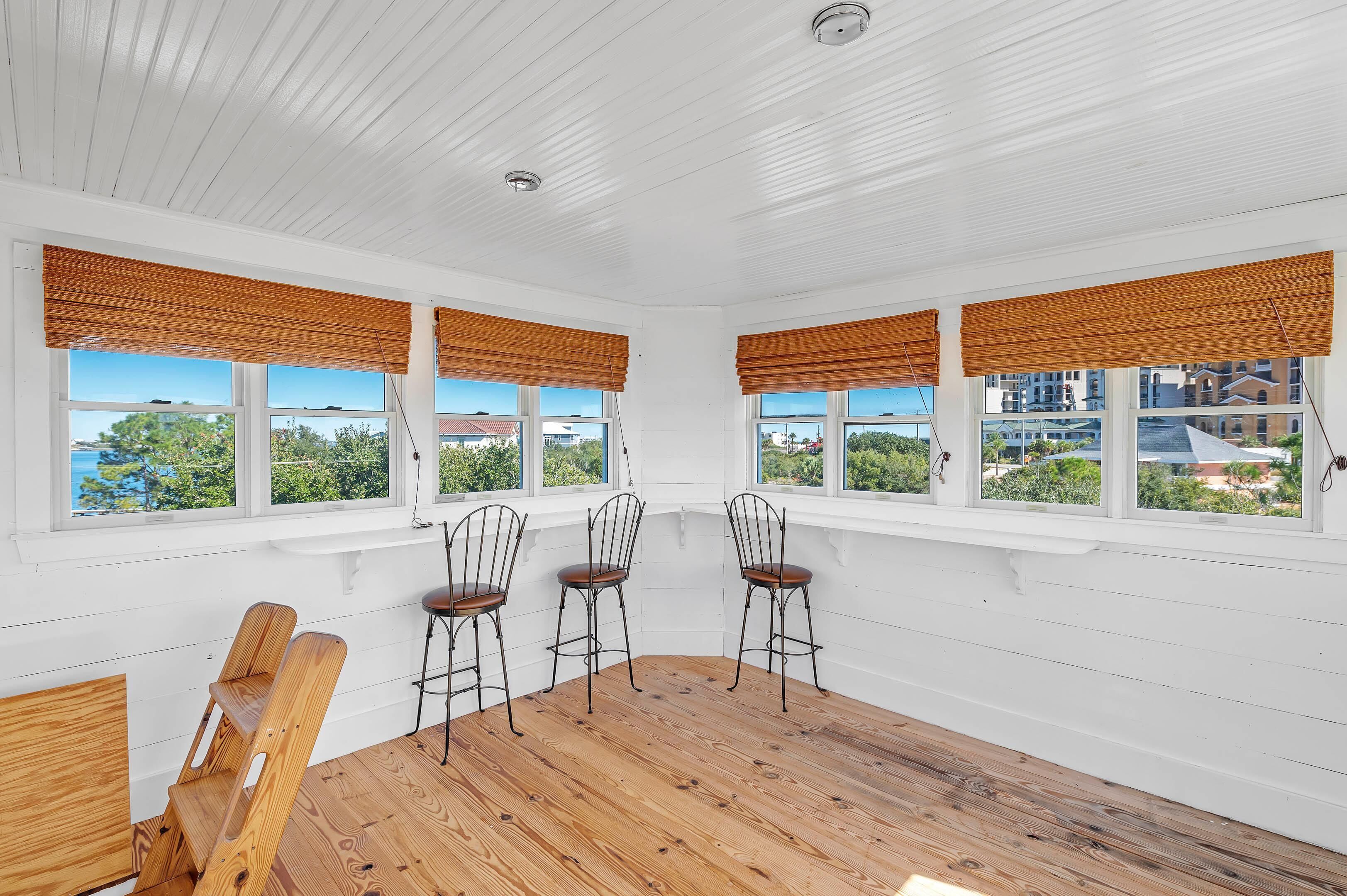 A room with white wooden walls, a wooden floor, and three metal chairs with wooden seats.