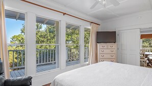 A bedroom with a large bed, a TV, a dresser, and a balcony with a railing. - Ole River Cottage (Pensacola)
