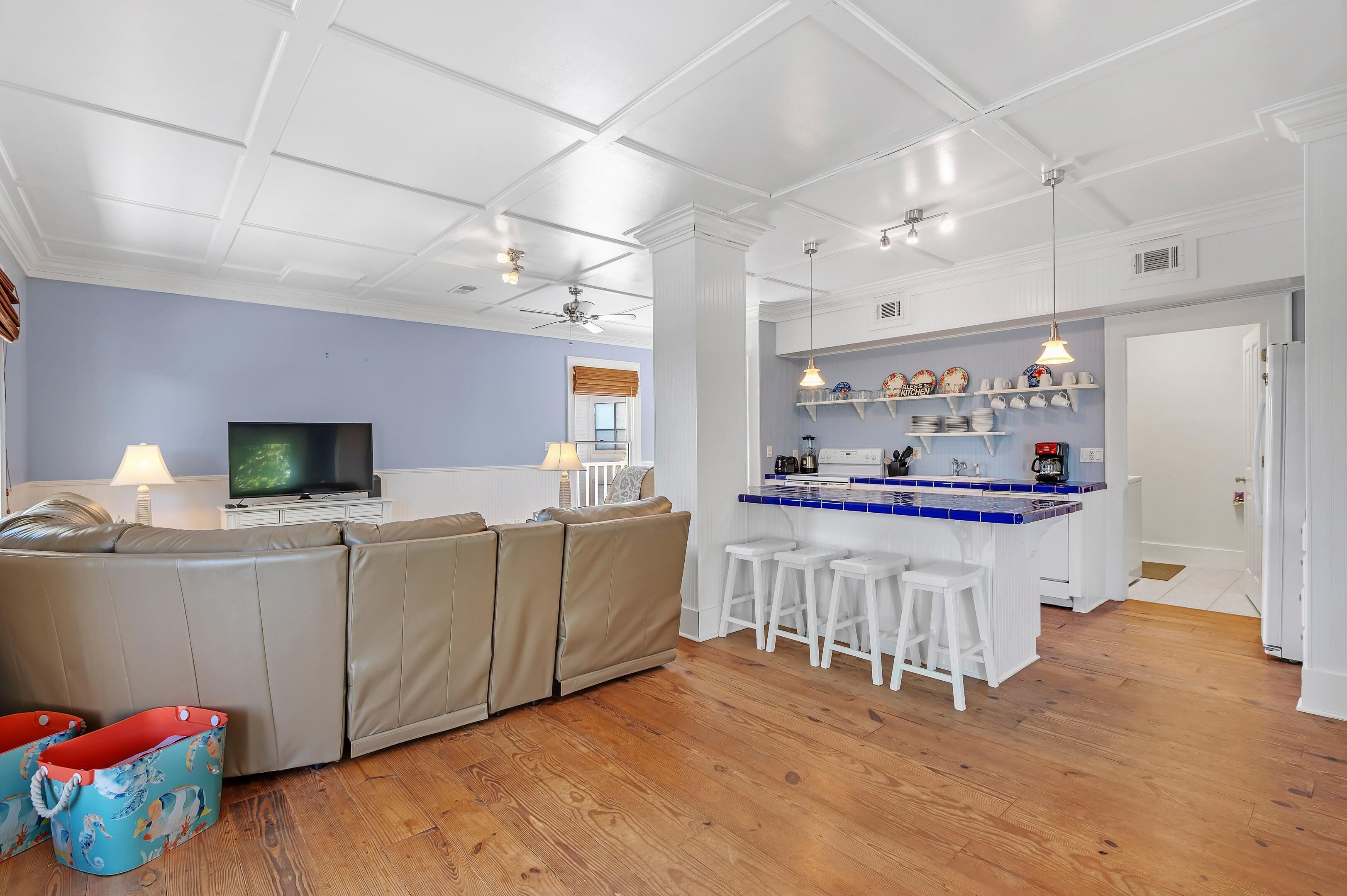 A modern living room with a sectional sofa, a TV, and a kitchen area with bar stools and shelves.