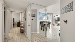 A modern interior with a glass partition, a dining area with chairs and a table, and a sign indicating 'Phoenix East 806 Beach House'. - Phoenix East 806 (Orange Beach)