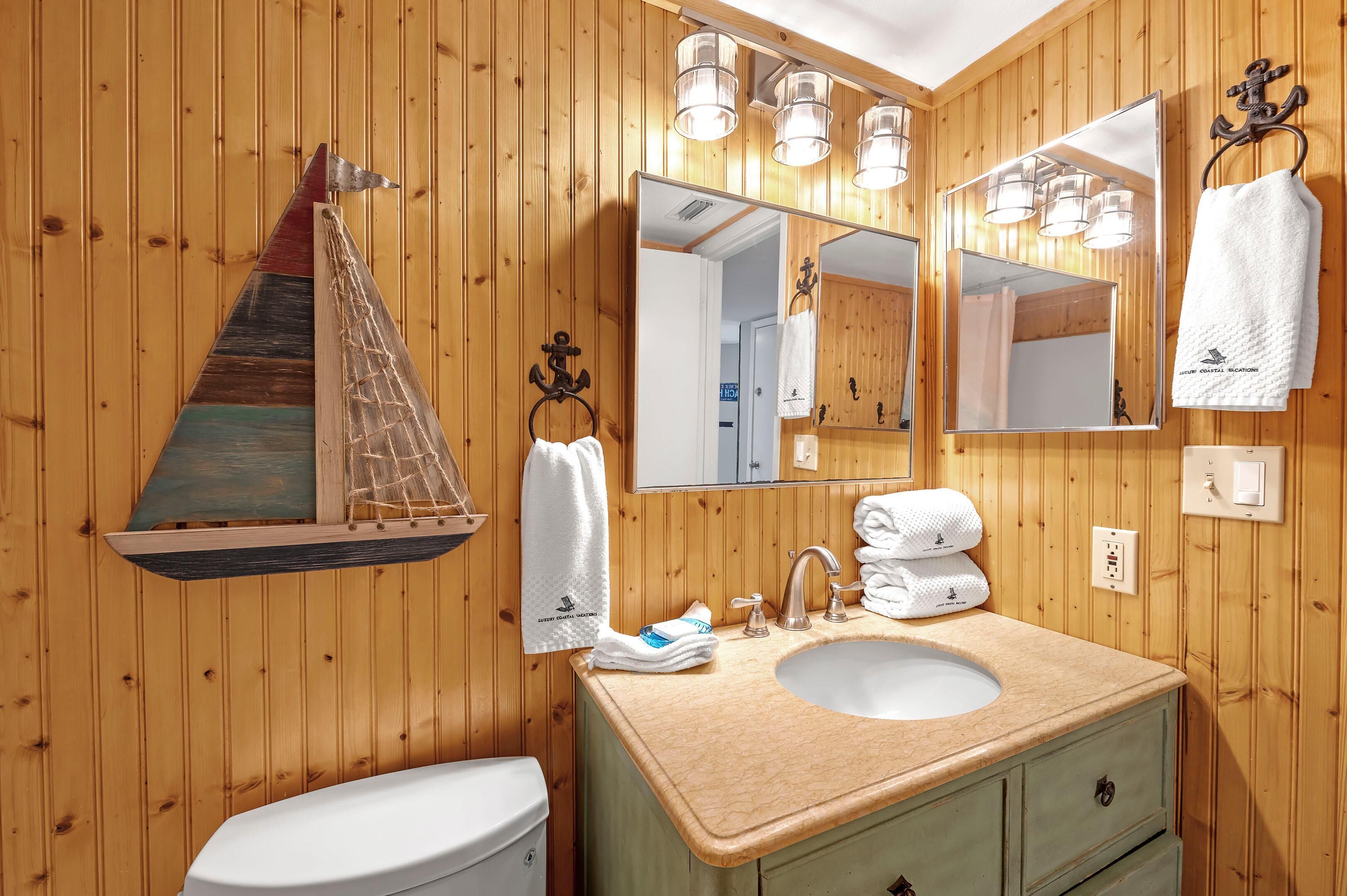 Un bagno con rivestimenti in legno, decorato con una nave in legno, uno specchio grande, un lavandino e un water.