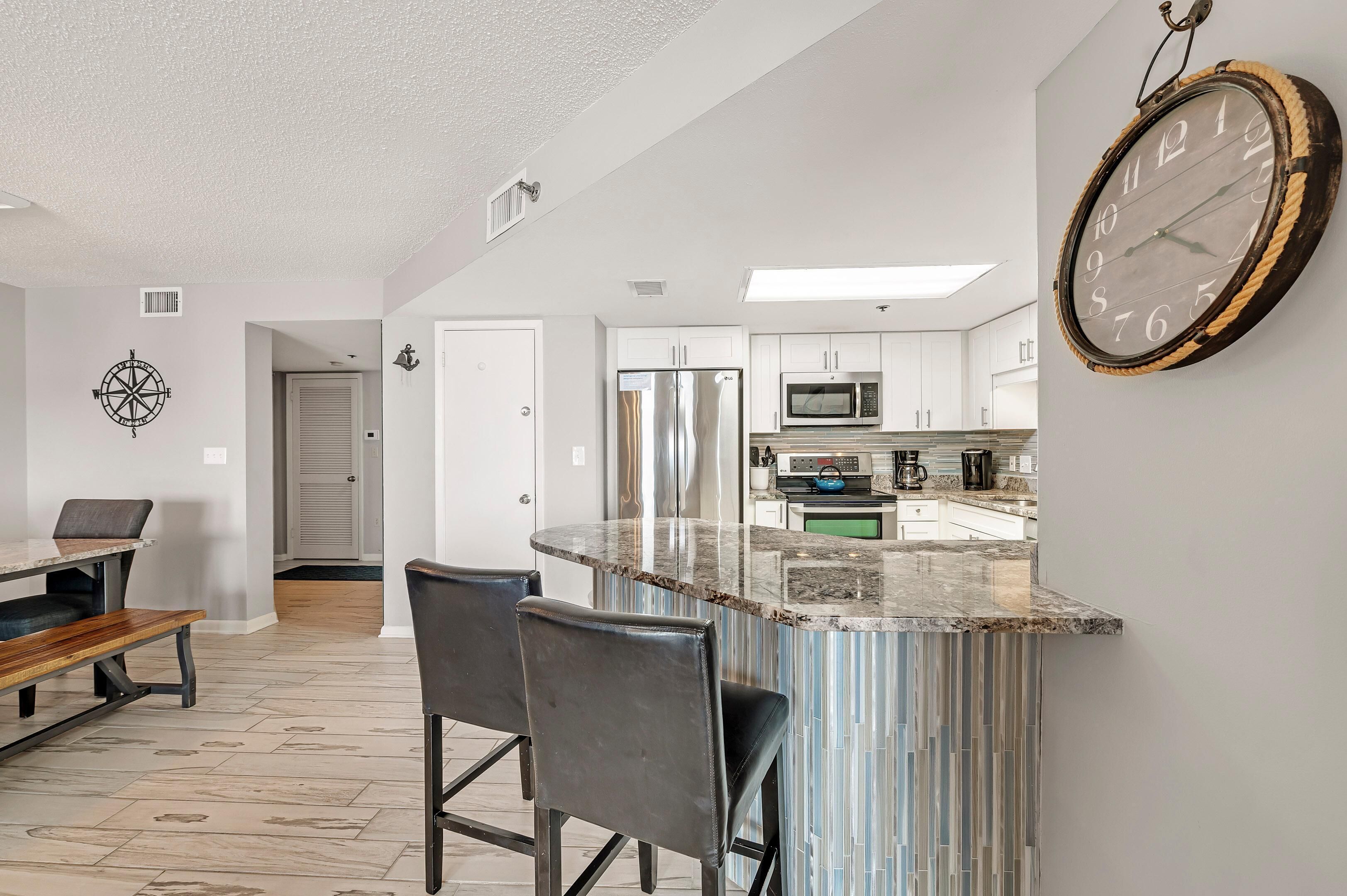 A modern kitchen with a central island, stainless steel appliances, and a large clock on the wall.