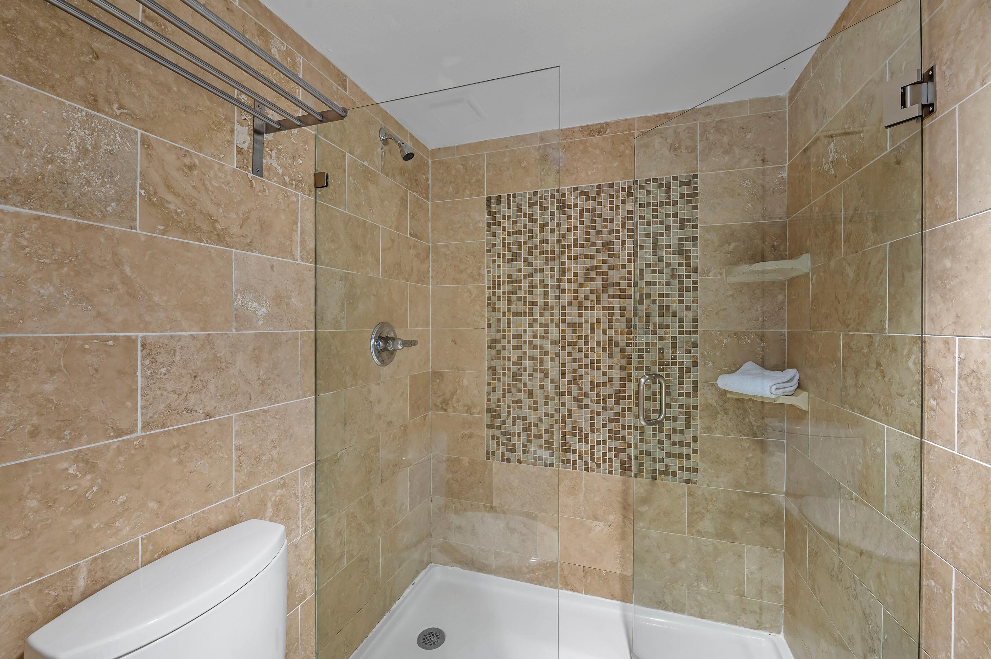 Een badkamer met een douche, toilet en betegelde wand.