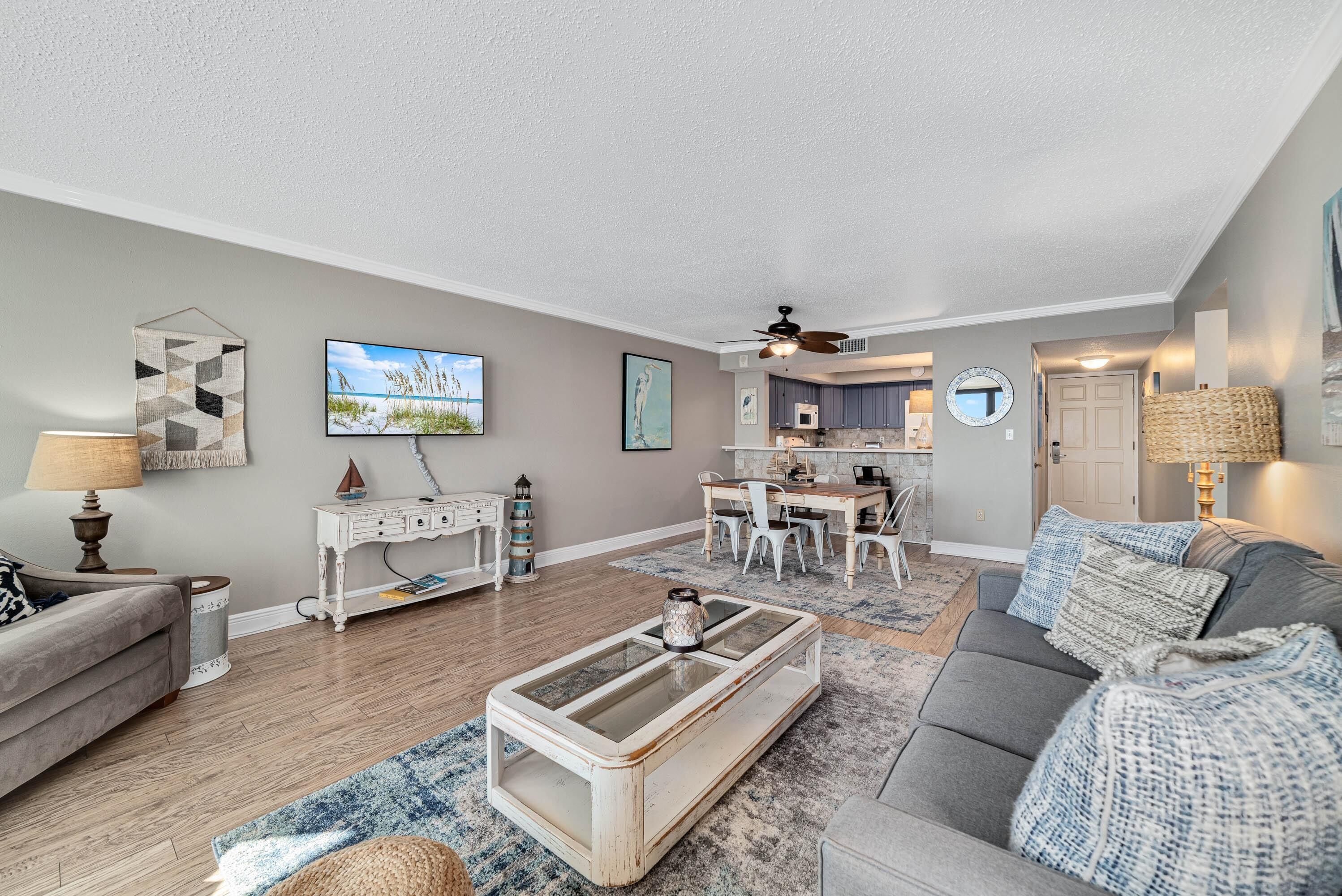 A spacious living room with a gray sofa, a coffee table, and a dining area with a white table and chairs.