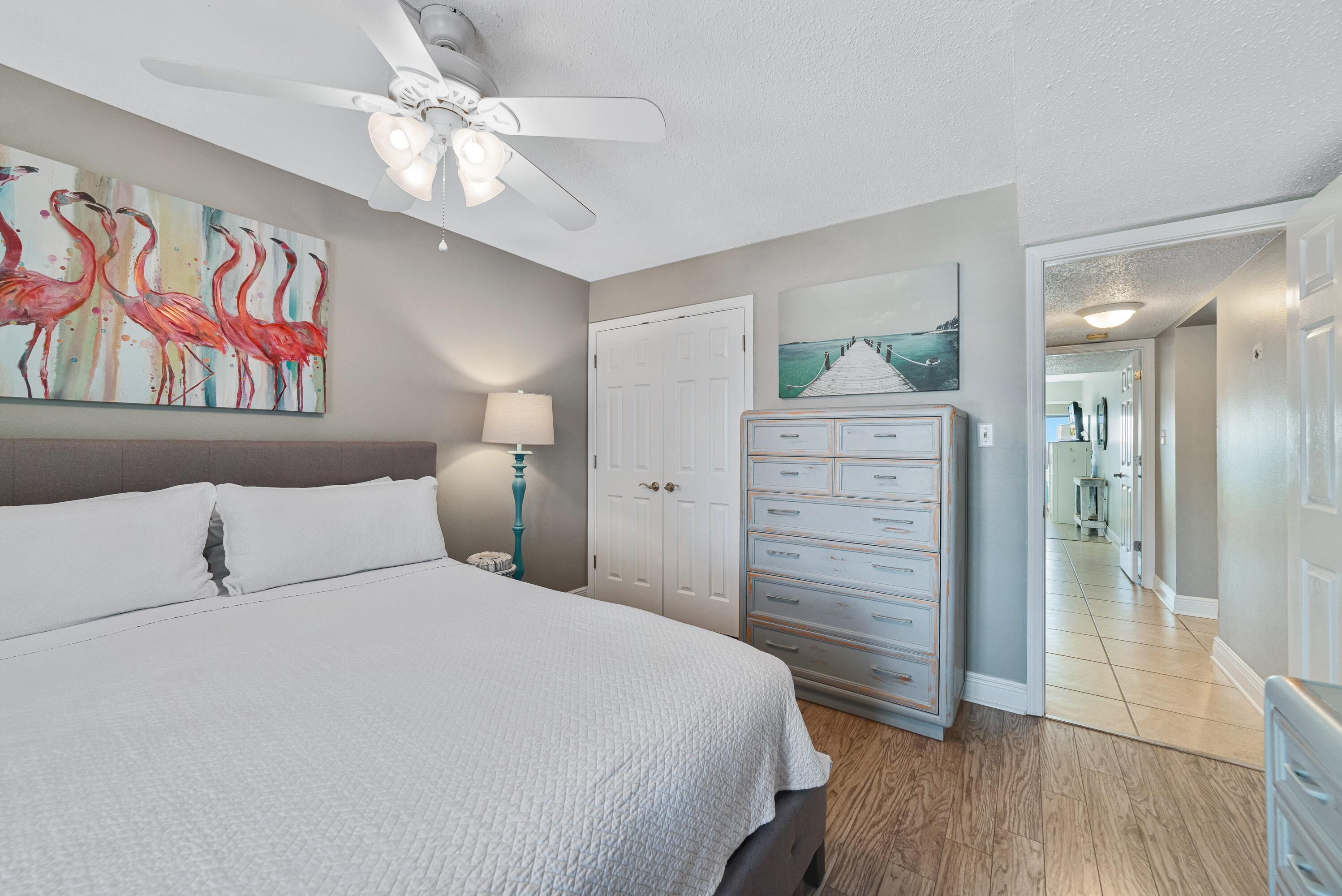 A bedroom with a bed, a ceiling fan, a dresser, and a door leading to another room.
