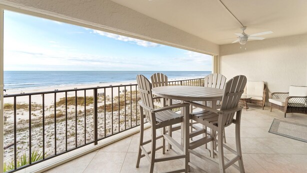 A balcony with a view of the beach, a table with chairs, and a ceiling fan. - Shipwatch A402 (Pensacola)