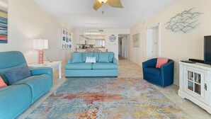 A living room with a ceiling fan, a sofa, a chair, and a TV on a cabinet. - Shipwatch A402 (Pensacola)