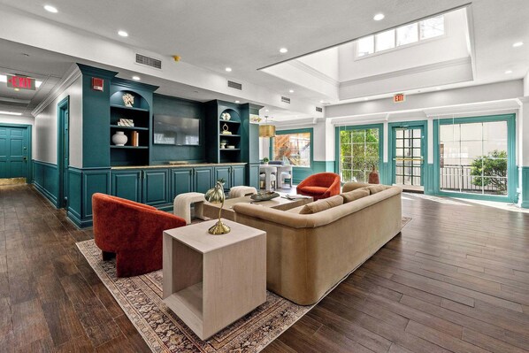 A spacious living area with a sofa, red chair, and a coffee table. There is a kitchen area with teal cabinets and a TV.