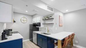A modern kitchen with white countertops, blue cabinets, and a central island with bar stools.