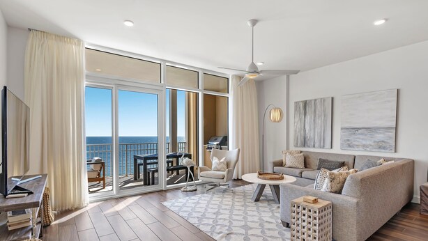 Ein geräumiges Wohnzimmer mit einer großen Glasschiebetür, die auf einen Balkon führt, einer Sofagarnitur, einem Couchtisch und einem Fernseher auf einem Holztisch.