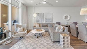 Ein modernes Wohnzimmer mit grauem Sofa, Sesseln, einem Couchtisch und einem Essbereich mit einer Chandelier.