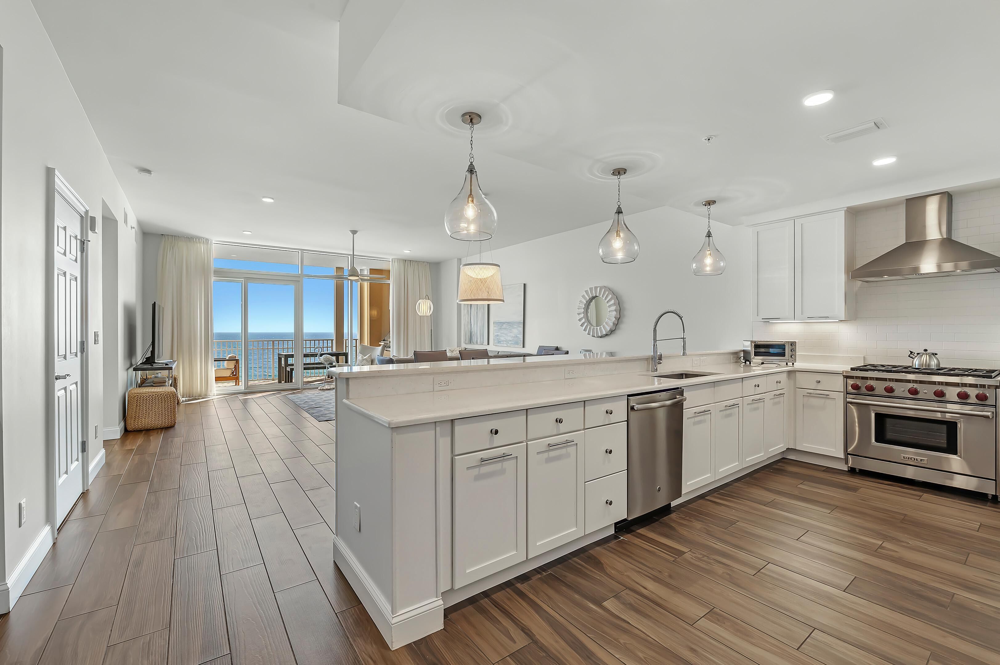 A modern kitchen with white cabinetry, a large island, stainless steel appliances, and pendant lighting.